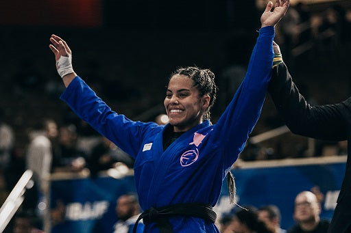 Martial artist in a blue gi with arms raised in victory, while a referee holds one arm up at a competition.