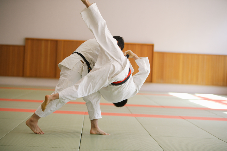 Two judo athletes in white gis practicing a hip throw technique on the mat.