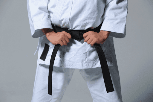 Martial artist wearing a white Gi and tying a black belt around the waist.