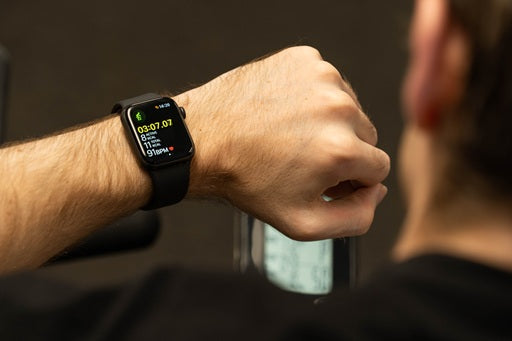 A close-up of a hand wearing a smartwatch displaying a workout timer and stats, with a blurred figure in the background.