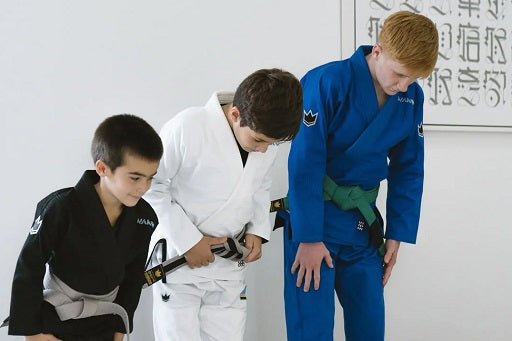 Three children wearing gi bowing in a BJJ setting, with Japanese calligraphy visible on the wall.