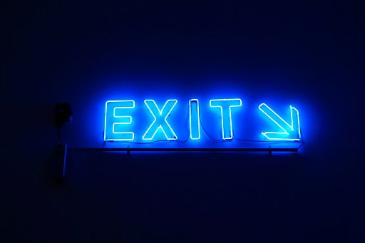 Blue neon "EXIT" sign with a right-pointing arrow glowing against a dark background.