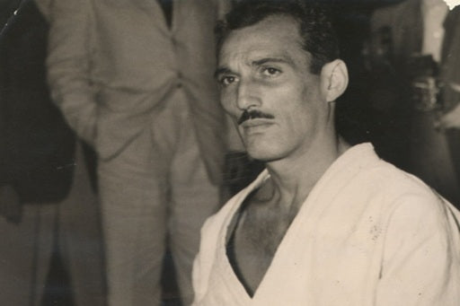 Hélio Gracie in a white gi with men in suits behind him in a black and white 1952 photo.