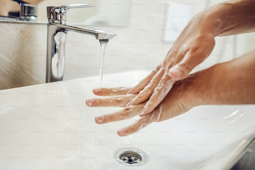 A person washes their hands with soap under running water at a bathroom sink, promoting hygiene and cleanliness.