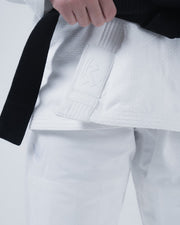 Kingz Born to Rule Women's Jiu Jitsu Gi - White - Close-Up Detail View Hand Holding Black Belt Embossed Kingz Logo Patch Textured Fabric Crown Badge Pants BJJ Gi Training [color:White]
