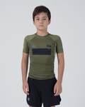 Kingz Trooper Youth Rashguard Military Green - Full Body Front View Young Boy Athlete Short Sleeve Olive Green Black Chest Band Flag Patches Gray Side Panels Black Shorts Kids BJJ