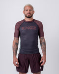 Kingz Noise V2 Rashguard Dark Gray Red - Full Body Front View Male Athlete Short Sleeve Dark Charcoal Body Red Rust Noise Static Dot Pattern Sleeves KINGZ Red Noise Text Matching Noise Pattern Shorts Crown Logo BJJ No-Gi Training