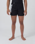 Kingz Kore 2.0 Women's Shorts Black - Full Body Front View Female Athlete Solid Black Bold Vertical KINGZ White Text Left Leg Circular Crown Badge Right Leg Black Elastic Waistband Competition Cut Women's Grappling Shorts No-Gi BJJ