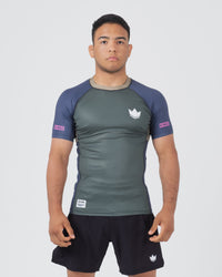 Kingz Draft Rashguard Storm Blue - Full Body Front View Male Athlete Short Sleeve Gray Charcoal Body Blue Raglan Sleeves White Crown Logo Pink KINGZ Labels Crown Badge Black Shorts [color:Storm Blue]