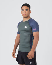 Kingz Draft Rashguard Storm Blue - Full Body 3/4 Angled Front View Male Athlete Short Sleeve Gray Body Blue Raglan Sleeves Crown Logo Pink KINGZ Sleeve Label Black Shorts Crown Badge [color:Storm Blue]