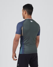 Kingz Draft Rashguard Storm Blue - Full Body 3/4 Back View Left Side Male Athlete Short Sleeve Gray Body Crown Logo Upper Back Blue Raglan Sleeves Teal Side Stripe Pink KINGZ Label Shorts [color:Storm Blue]