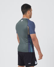 Kingz Draft Rashguard Storm Blue - Full Body 3/4 Back View Right Side Male Athlete Short Sleeve Crown Logo Back Blue Raglan Sleeves Teal Side Stripes Gray Body KINGZ Badge Shorts [color:Storm Blue]
