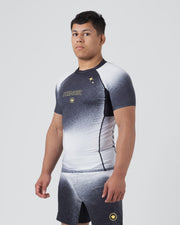 Kingz Galaxy Rash Guard Black White - Full Body 3/4 Front Left Side View Male Athlete Short Sleeve Black To White Ombre Galaxy Spatter Pattern KINGZ Gold Text Gold 4-Point Star Crown Logo Matching Galaxy Shorts [color:Black/Galaxy]