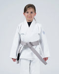 A young girl wearing a white martial arts gi with a gray belt, standing against a light gray studio background.