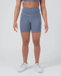 Kingz Kore Women's Training Shorts Smoke Blue Steel Blue - Full Body Front View Female Athlete Steel Blue Biker Style Short Cut High-Waist Wide Waistband Side Pocket Light Contrast Stitching KINGZ White Text Right Outer Thigh Matching Steel Blue Sports Bra White Sneakers Women's Training Shorts No-Gi BJJ Kore Collection [color:Steel Blue]