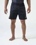 Kingz MI-K Roots Onça Pintada Shorts Black - Full Body Front View Male Athlete Dark Charcoal Black KINGZ Gold Vertical Text Left Leg MI-K Circular Crown Badge Right Thigh Subtle Texture Competition Cut Men's Grappling Shorts No-Gi BJJ MI-K Roots Jaguar Collection